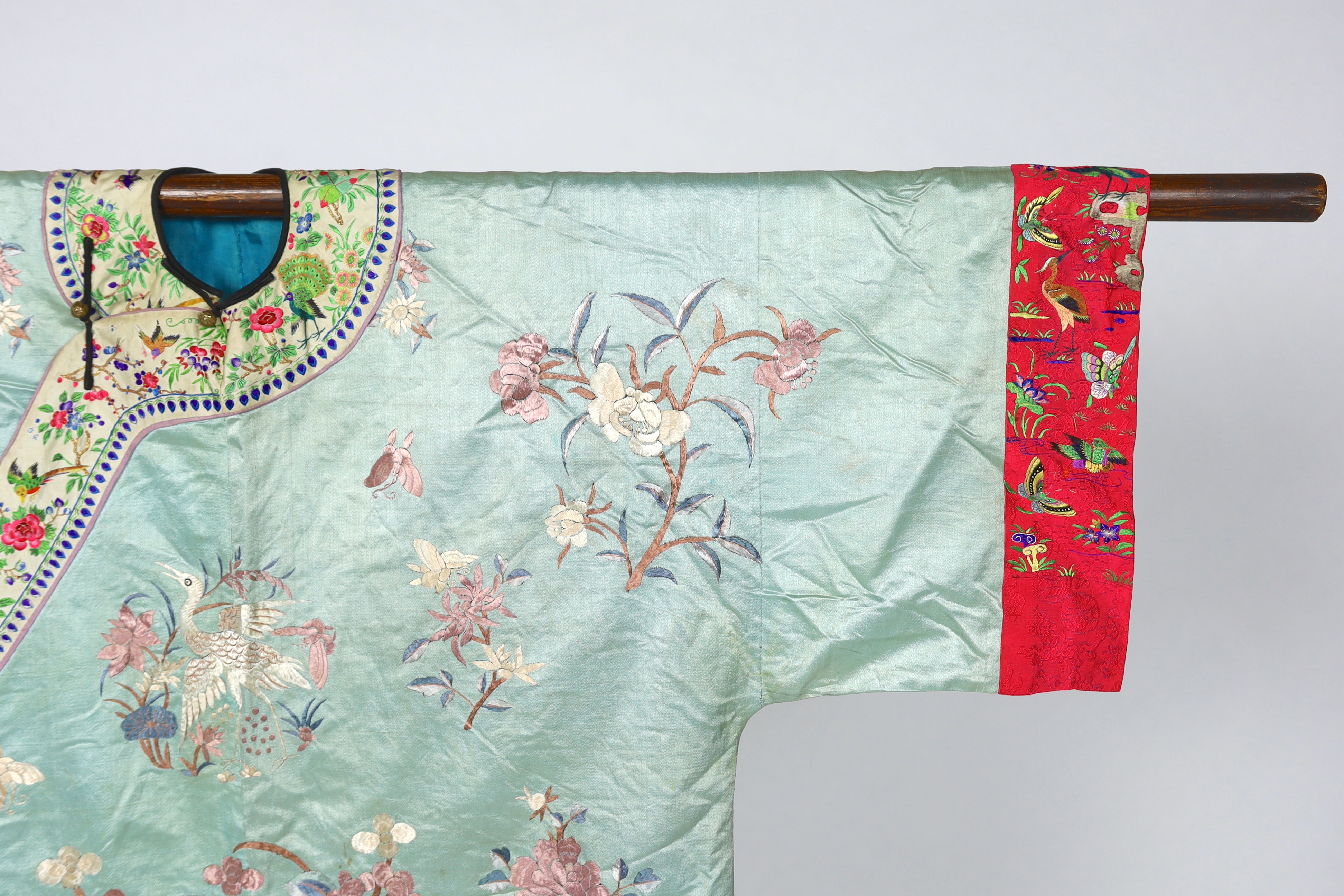 An early 20th century Chinese silk embroidered turquoise robe, embroidered in pastel silk with butterflies and flowers all over, polychrome embroidered braiding edged with lilac and bright pink sleeve bands embroidered w